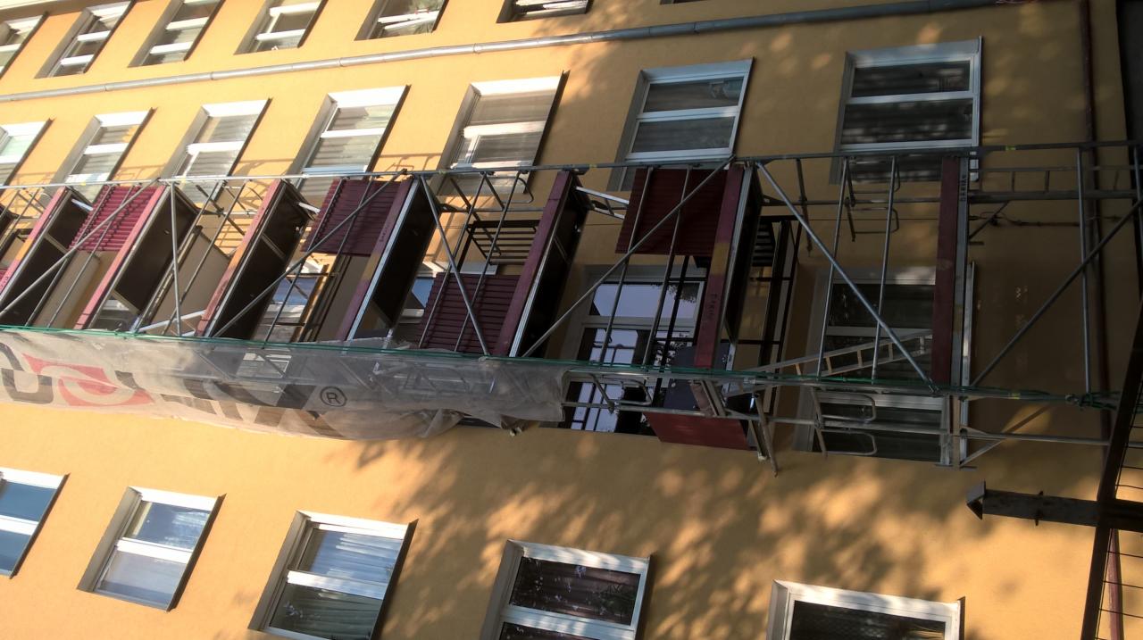 Budynek w trakcie montażu okien, widoczne rusztowania i elementy okienne z zewnątrz.