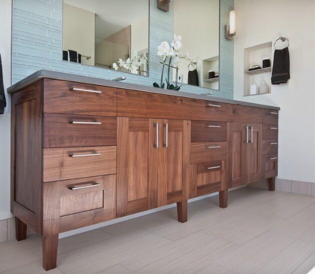 Długa, drewniana szafka łazienkowa z szufladami i szafkami, zwieńczona szarym blatem, podwieszona pod dwoma lustrami z niebieską mozaiką i białymi orchideami.