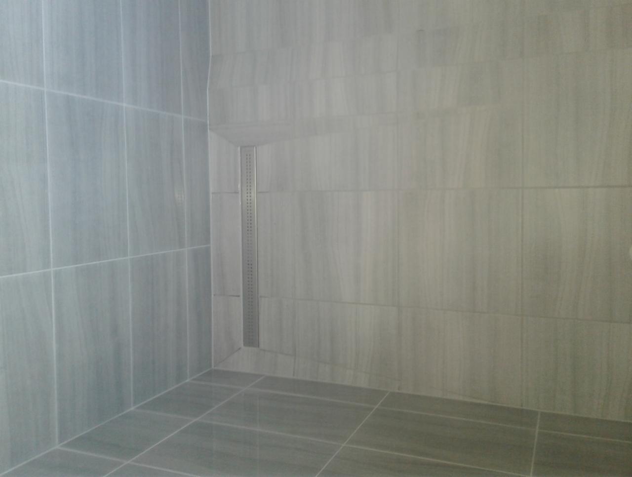 Wykończona kabina prysznicowa z szarymi płytkami imitującymi drewno i liniowym odpływem.