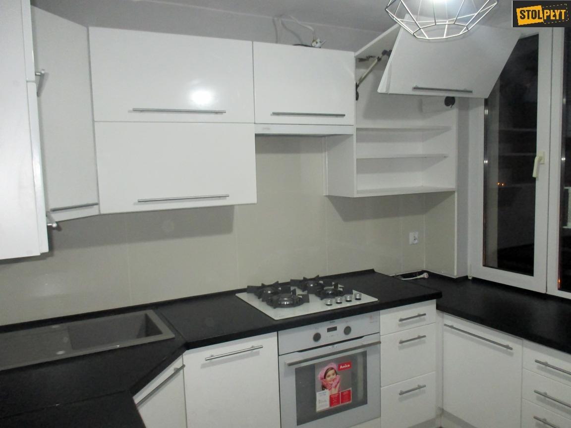 Nowoczesna kuchnia z białymi szafkami i czarnym blatem, widoczna płyta gazowa i piekarnik Amica, oświetlenie sufitowe w geometrycznym stylu.