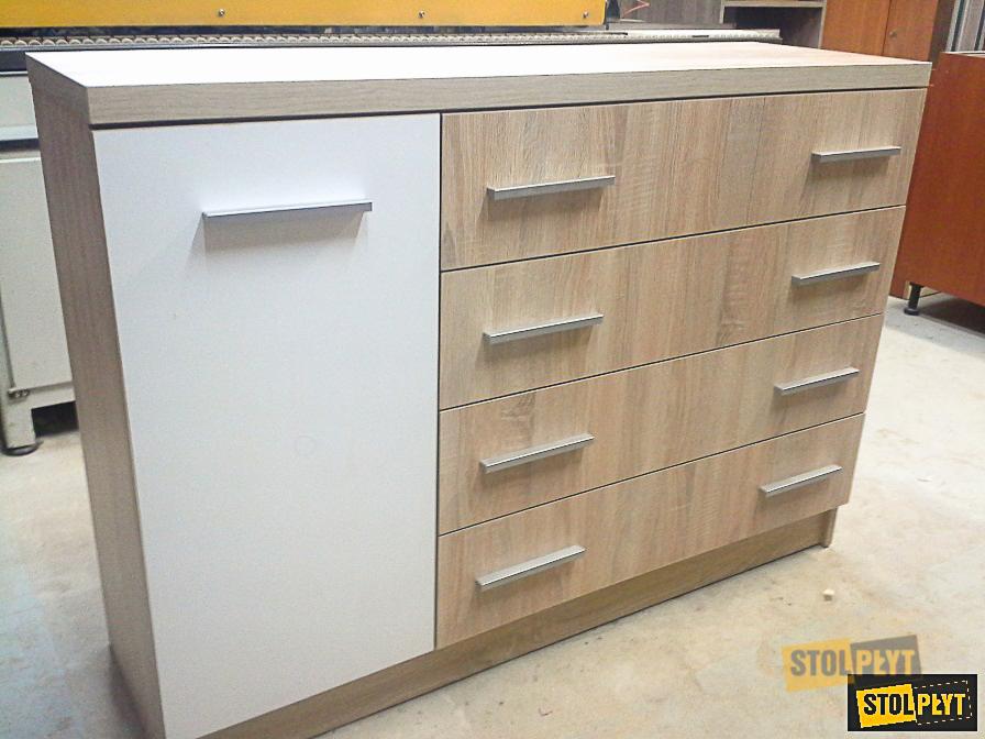 Komoda na wymiar z czterema szufladami w kolorze jasnego drewna i białymi drzwiczkami, z podłużnymi srebrnymi uchwytami, widoczna z boku, w tle warsztat.