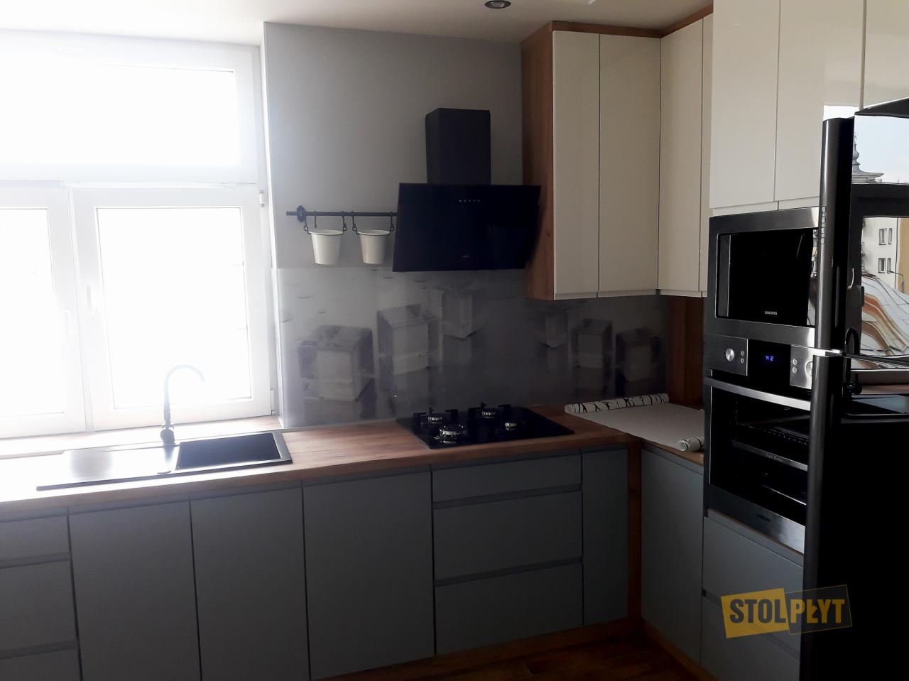 Szara kuchnia z drewnianym blatem, czarnym okapem i kuchenką, z grafiką kryształowych sześcianów na ścianie, oraz białymi szafkami górnymi.