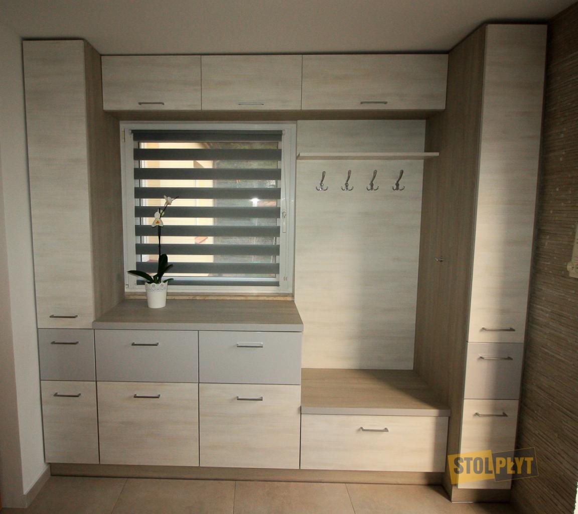 Zabudowa przedpokoju z szafkami, siedziskiem i wieszakami w jasnej kolorystyce, zrealizowana na wymiar w Krasnystawie, widoczna roślina w doniczce na parapecie.