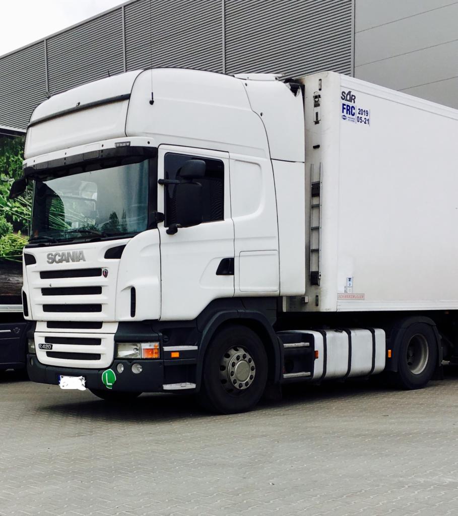 Biała ciężarówka Scania R420 z naczepą chłodniczą zaparkowana na betonowym placu, widoczna drabinka na naczepie i oznaczenia SQR FRC 2019 05-21.