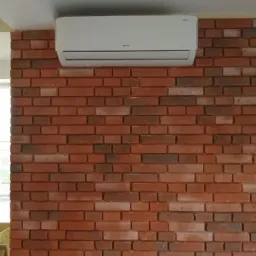 Biały klimatyzator ścienny zamontowany na ceglanej ścianie w Jakubowie, widok z przodu.