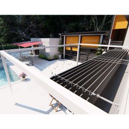 Artbegstudio- - Nowoczesna pergola z regulowanym zadaszeniem lamelowym w minimalistycznym ogrodzie z basenem i widokiem na budynek z pomarańczowymi osłonami okiennymi.