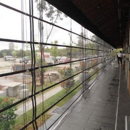 Artbegstudio- - Przezroczyste osłony przeciwwietrzne z czarnymi poprzeczkami na zewnątrz budynku, widok na parking i ulicę w pochmurny dzień.