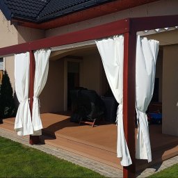 Artbegstudio- - Pergola z brązowego drewna z białymi zasłonami na tarasie, widok z zewnątrz, osoba z drabiną w tle.