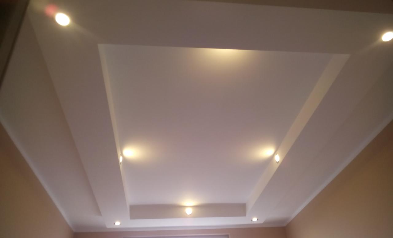 Sufit podwieszany z oświetleniem punktowym LED, widok z dołu, kremowe ściany w tle.