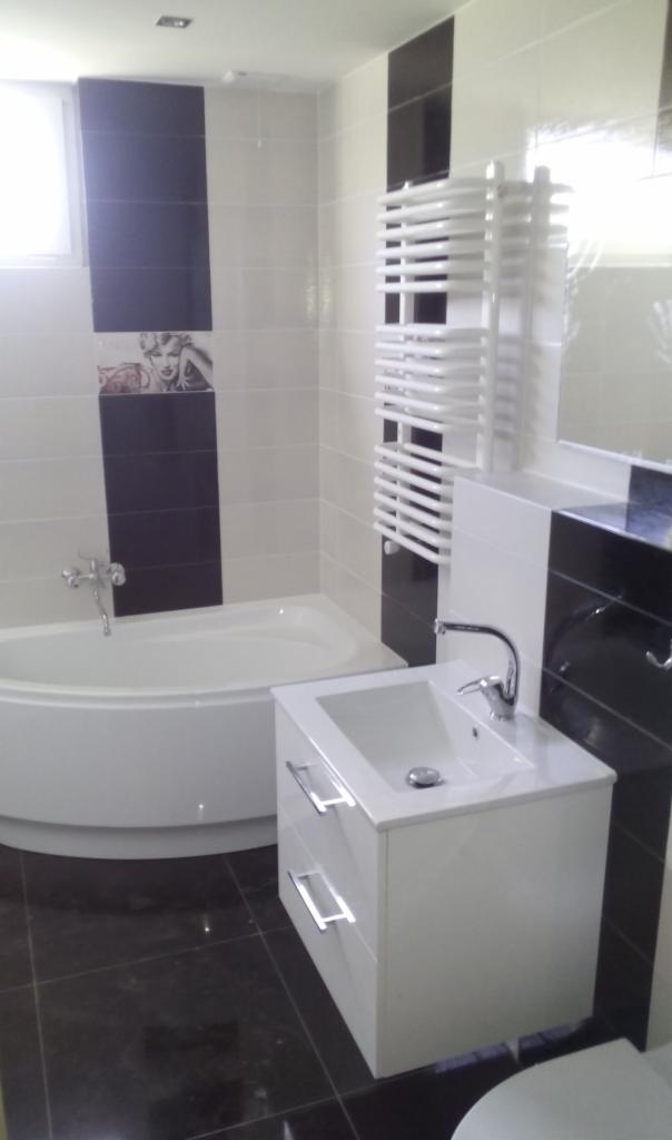 Biało-czarna łazienka z wanną narożną, grzejnikiem drabinkowym i szafką pod umywalkę z dwiema szufladami, płytki z motywem Marilyn Monroe.