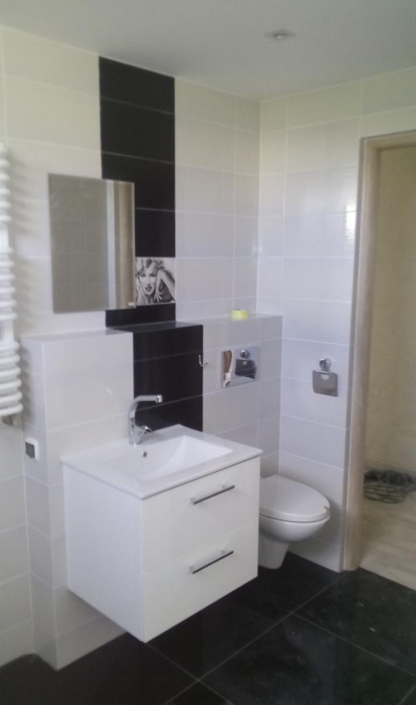 Biało-czarna łazienka z umywalką na szafce, lustrem, toaletą i czarną podłogą z płytek; na ścianie dekoracyjny panel z wizerunkiem kobiety.