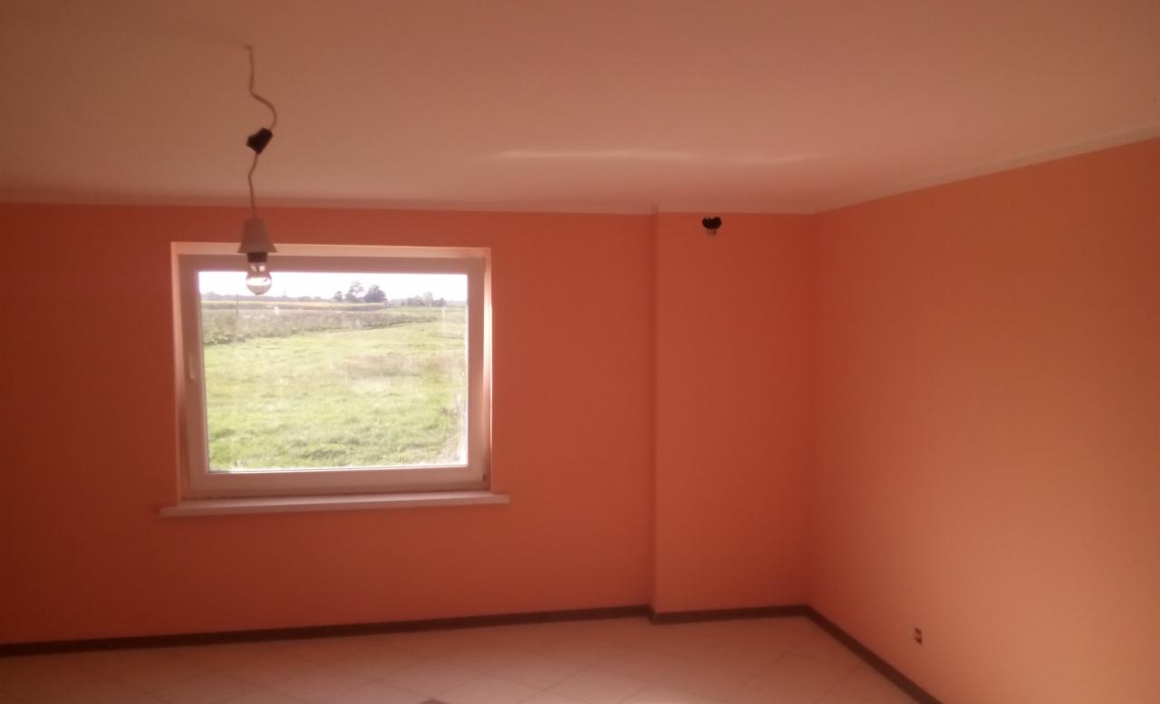 Pomarańczowy pokój po malowaniu ścian, widok na zewnątrz przez okno, surowa żarówka zwisająca z sufitu, płytki podłogowe.