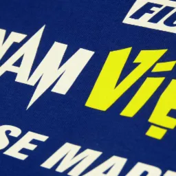 Zbliżenie niebieskiej koszulki z nadrukiem w kolorze białym i żółtym, przedstawiającym napisy w stylu grafiki sportowej.