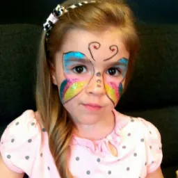 Dziewczynka z pomalowaną twarzą w motylka, z brokatem, w różowej bluzce w szare kropki i opaską na włosach.