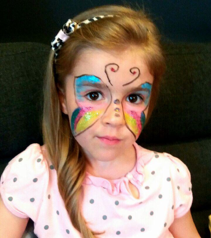 Dziewczynka z pomalowaną twarzą w motylka, z brokatem, w różowej bluzce w szare kropki i opaską na włosach.