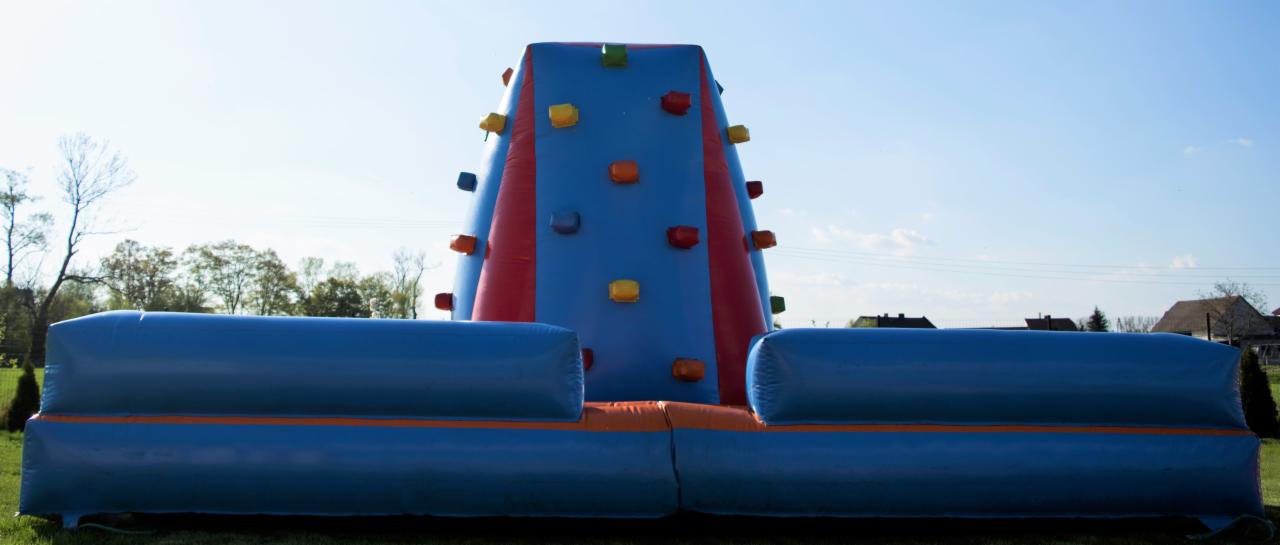 Niski kąt ujęcia dmuchanej ścianki wspinaczkowej z kolorowymi uchwytami, ustawionej na trawie w plenerze.