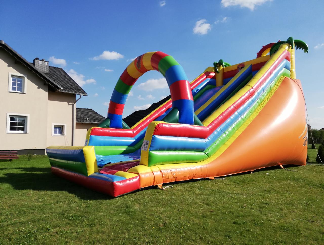 Kolorowa, dmuchana zjeżdżalnia z motywem dżungli, ustawiona na trawniku w Pawłowiczkach, z widocznym budynkiem mieszkalnym w tle pod błękitnym niebem.