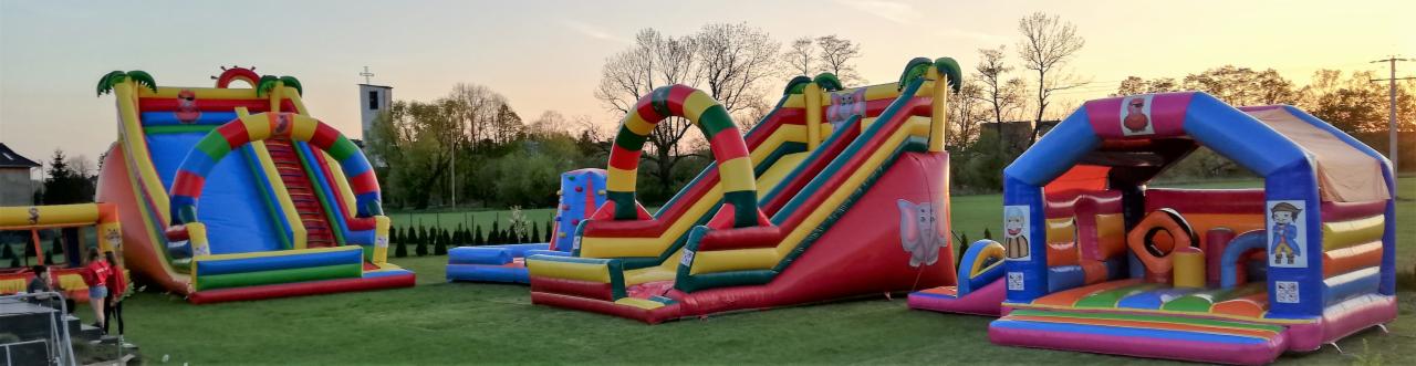Kompleks dmuchańców na trawie: zjeżdżalnie z motywem pirackim i dżungli, zamek z postaciami, w tle kościół.