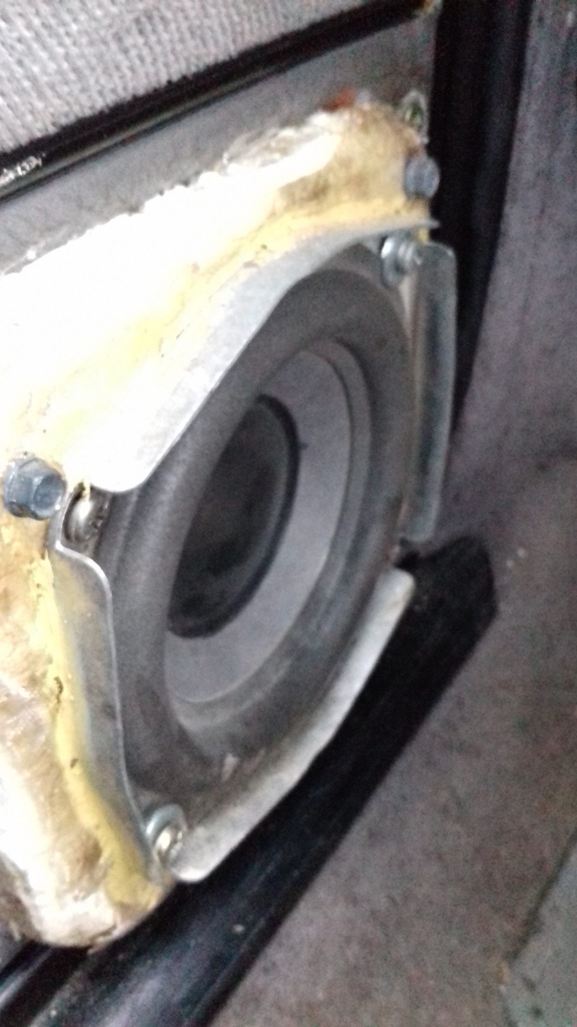 Głośnik niskotonowy zamontowany w obudowie, widoczne śruby mocujące i elementy instalacji wewnątrz pojazdu. Detal naprawy lub instalacji car audio.