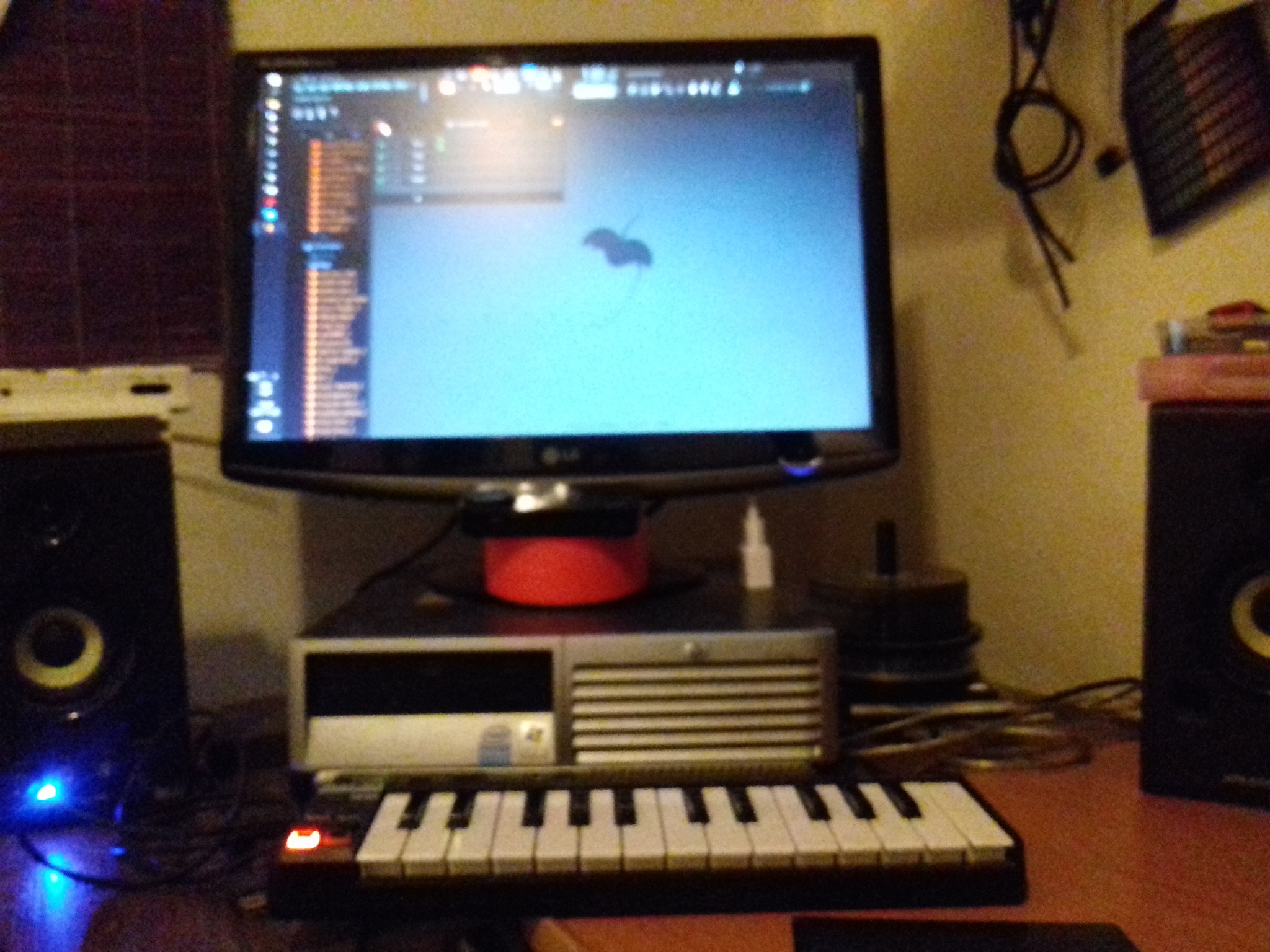 Stanowisko komputerowe z monitorem LG, klawiaturą MIDI i głośnikami studyjnymi. Na ekranie widoczny interfejs programu do produkcji muzyki.