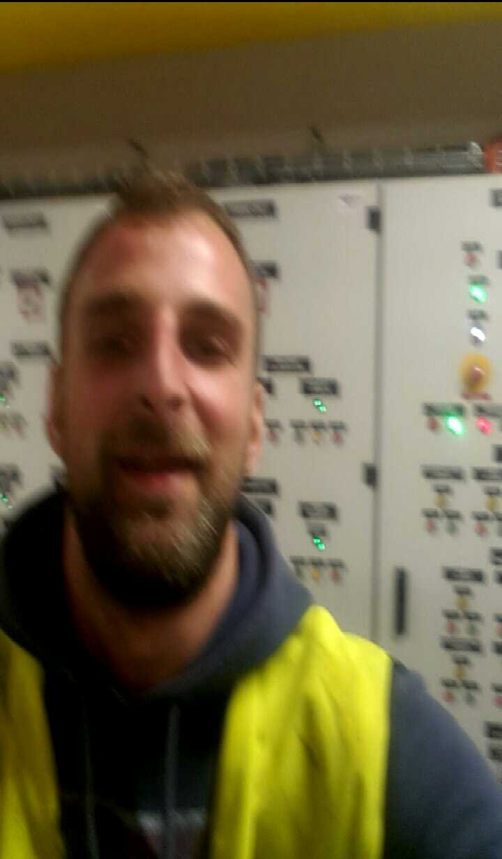 Mężczyzna w kamizelce odblaskowej na tle szafy sterowniczej z diodami w Kartuzach. Może to być serwisant lub elektryk.