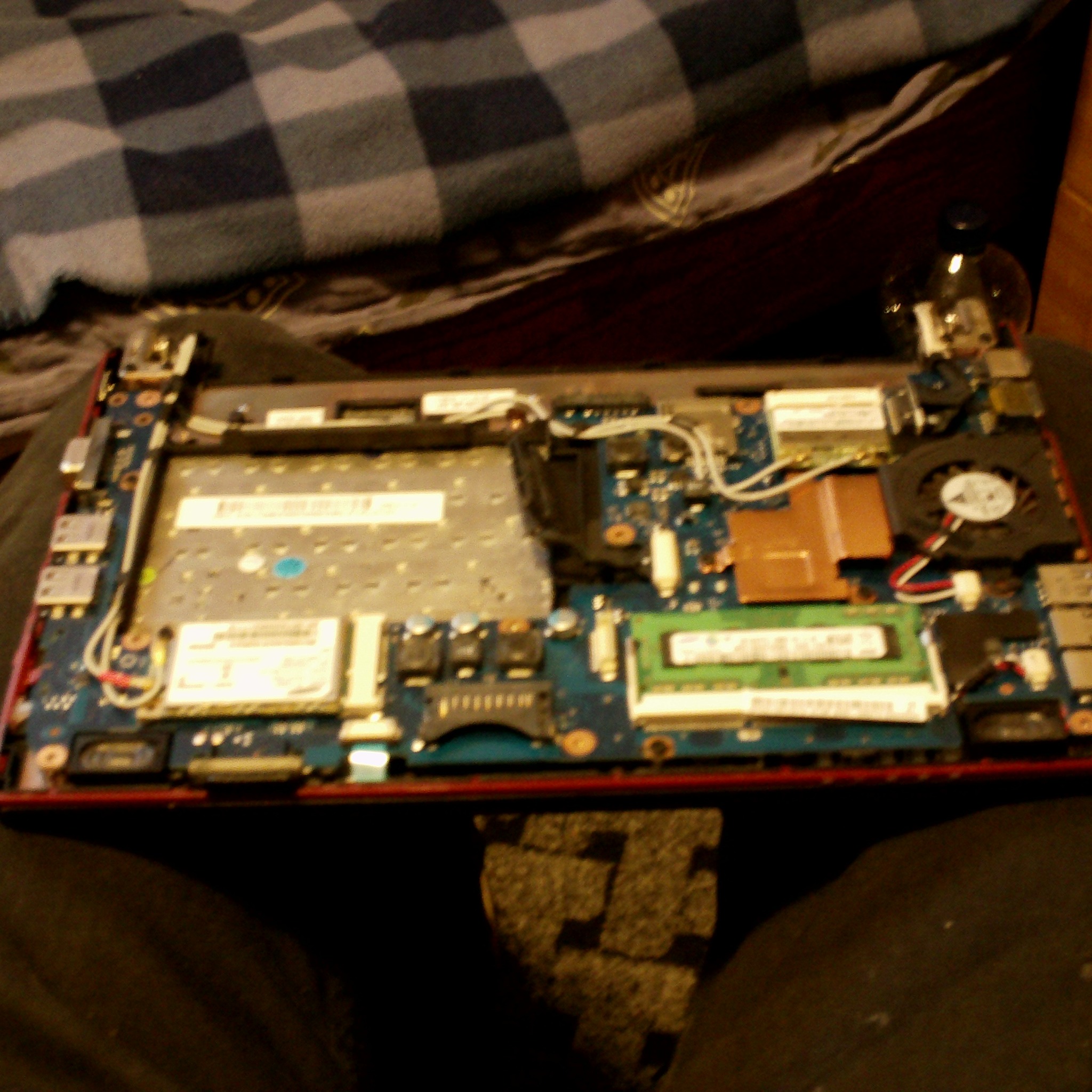 Wnętrze otwartego laptopa z widoczną płytą główną, elementami chłodzenia i pamięcią RAM. Widoczne ślady naprawy lub konserwacji.