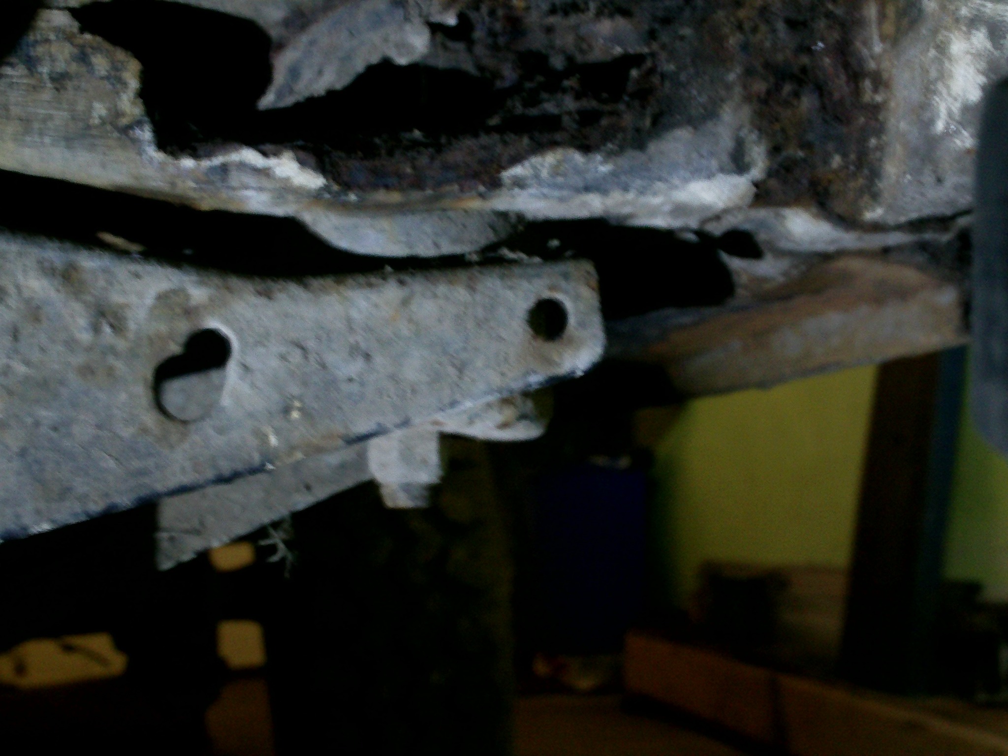 Nierówna, skorodowana powierzchnia metalowa z otworami i śladami napraw, prawdopodobnie fragment podwozia lub element konstrukcyjny w trakcie renowacji.