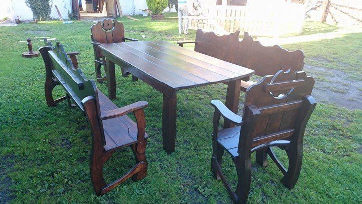 Drewniany komplet mebli ogrodowych: stół i ławki z oparciami, stylizowane na rustykalne, ustawione na trawniku.