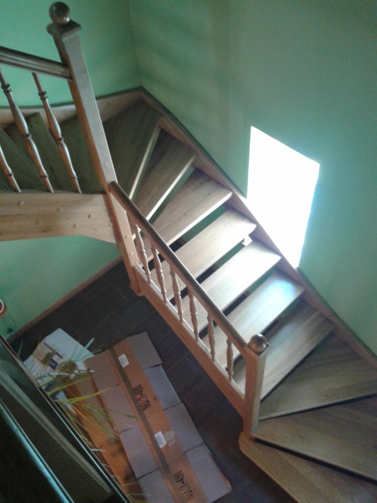 Wysoki kąt ujęcia na drewniane schody z balustradą w domu w Gozdnicy, widoczne kartony na podłodze i zielone ściany.