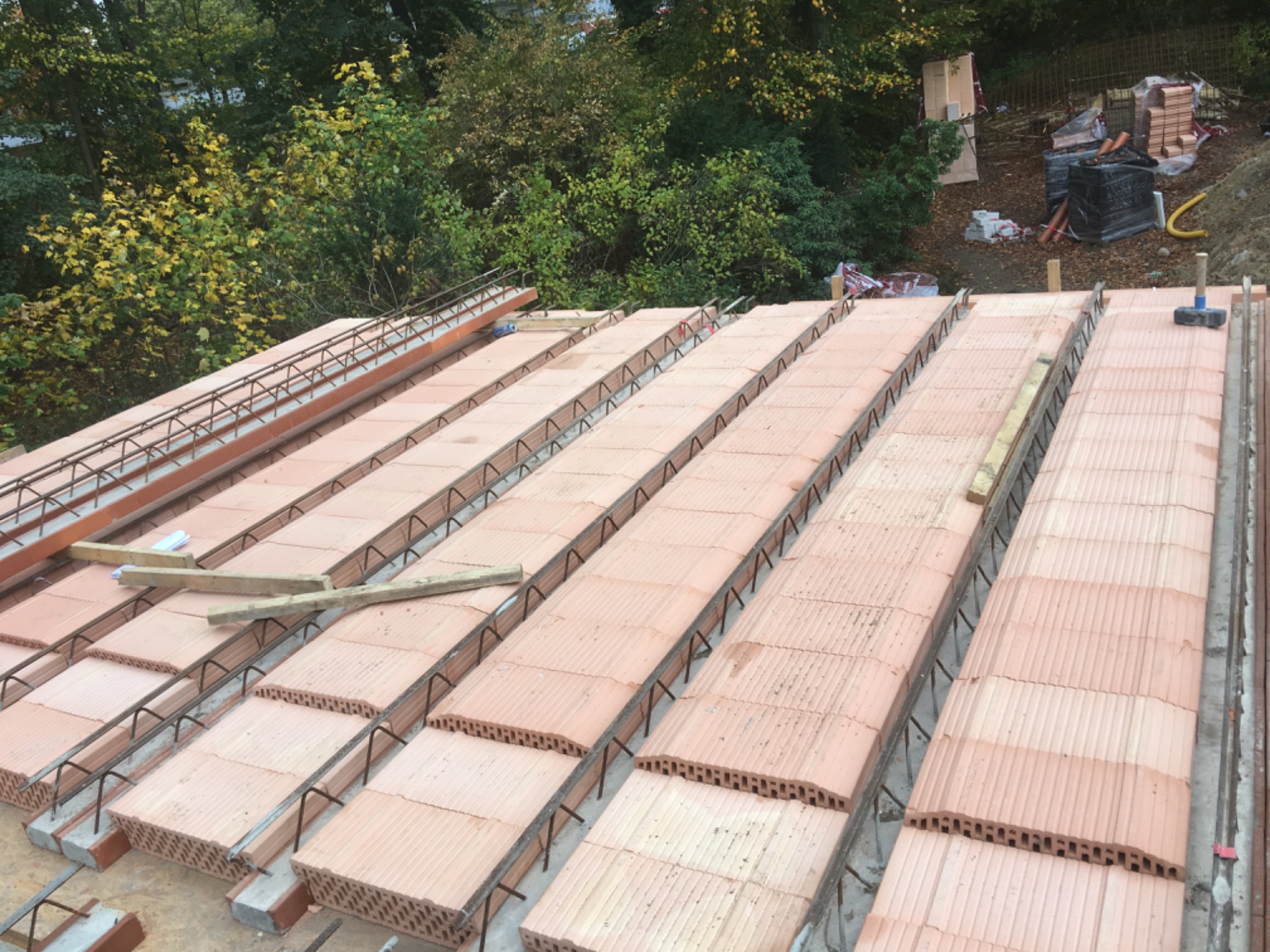 Wieniec stropowy w trakcie budowy, widoczne kształtki wieńcowe z betonu komórkowego zbrojone stalą, na tle drzewa i materiałów budowlanych.