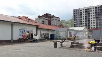 Prace brukarskie przed budynkiem sklepu LIDL; widoczny pracownik w żółtej kamizelce tnący kostkę brukową na palecie, biała elewacja budynku z reklamami i zaparkowany van.