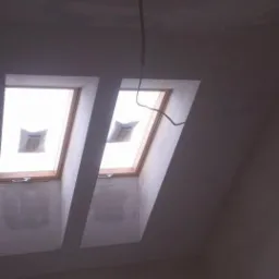 Poddasze ze świeżo osadzonymi oknami dachowymi, ściany w trakcie szpachlowania, widoczne niedoskonałości powierzchni przed malowaniem.