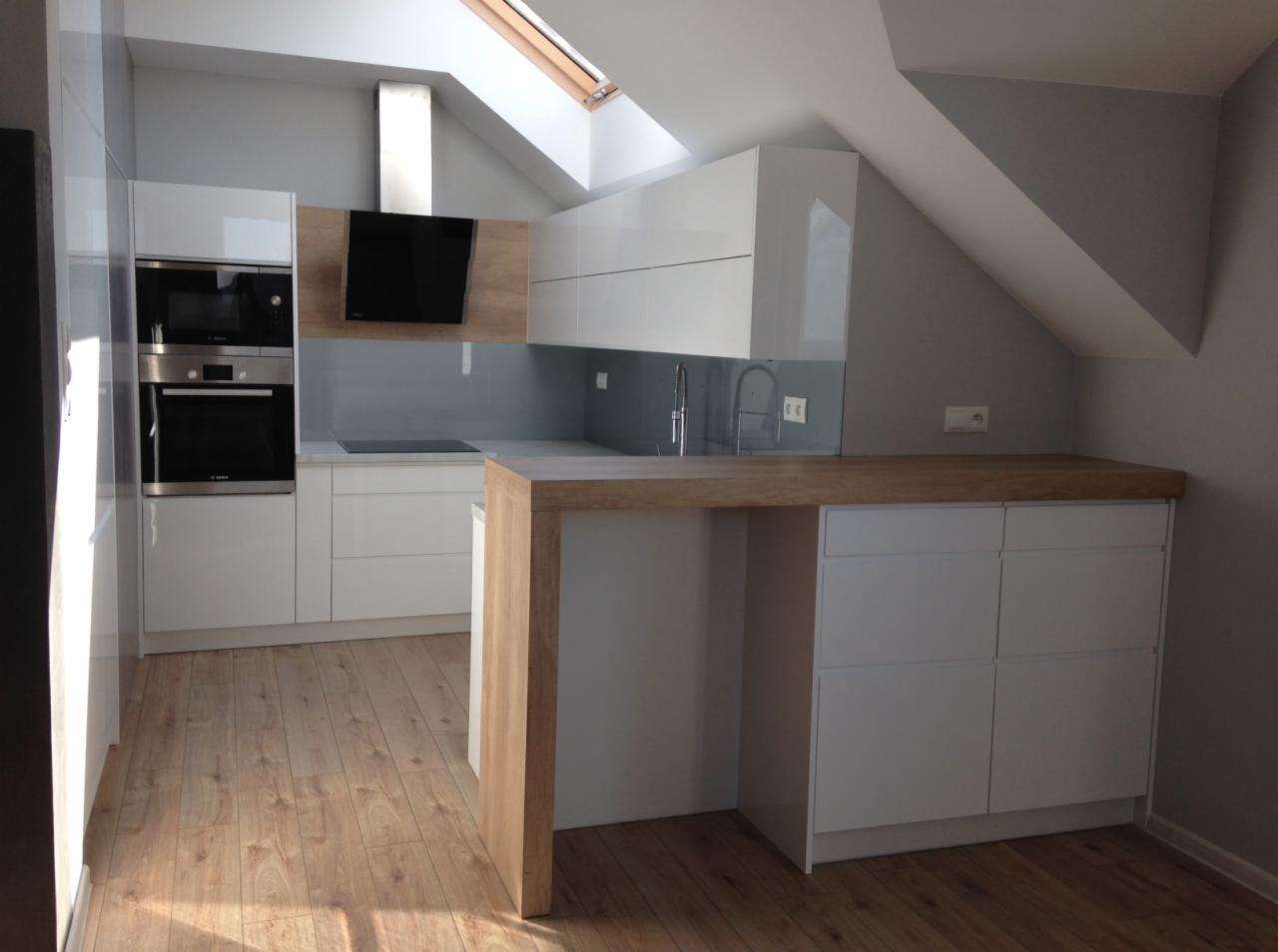 Nowoczesna kuchnia w odcieniach bieli i drewna z oknem dachowym, minimalistyczny design, zabudowa pod skosem, drewniany blat z półwyspem.