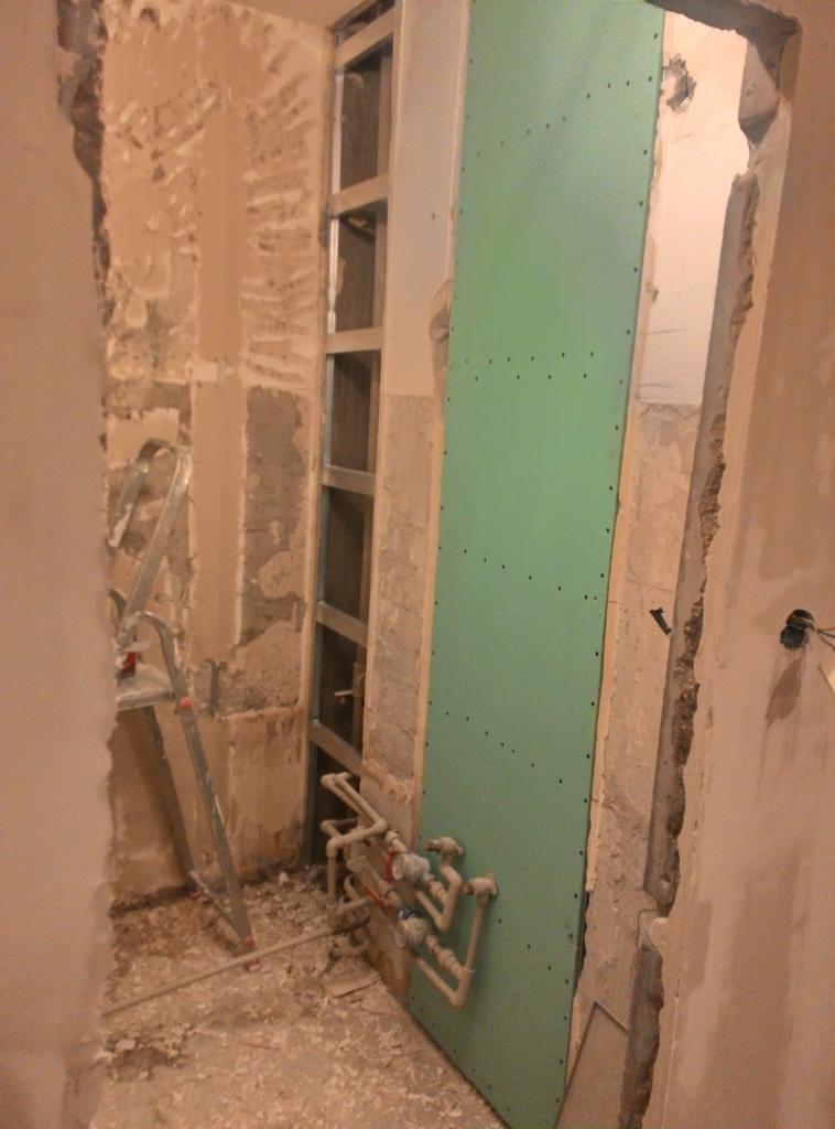 Remont łazienki w trakcie: widoczne metalowe profile, zielona płyta karton gips, instalacja wodna, ściany w stanie surowym i drabina.