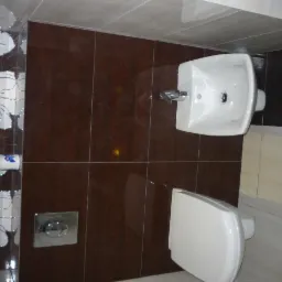 Ukończona łazienka z brązowymi płytkami, umywalką z baterią i wiszącą toaletą, akcentem są płytki z motywem kwiatowym na ścianie.