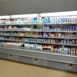 Pełna chłodziarka sklepowa z różnorodnym asortymentem nabiału, w tym mleka, jogurty i sery, z widocznymi regulatorami temperatury na dole.