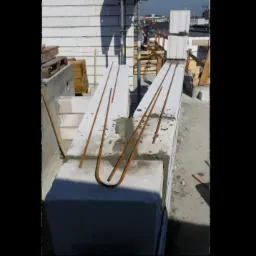 Wznoszenie ścian z bloczk&oacute;w betonowych z widocznym zbrojeniem pionowym na budowie, przy słonecznej pogodzie.