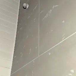 Ściana z płyt kartonowo-gipsowych po szpachlowaniu, widoczne łączenia i ślady szpachli, biała lampa sufitowa, biała boazeria na suficie.