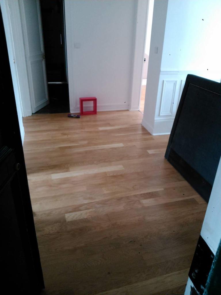 Jasne panele podłogowe w odnowionym wnętrzu z białymi ścianami, widok na otwarte drzwi i czerwony element dekoracyjny.