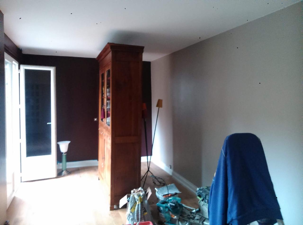 Pokój w trakcie odświeżania: ściana pomalowana na szaro, widoczny drewniany kredens, narzędzia malarskie i niebieska plandeka na podłodze.