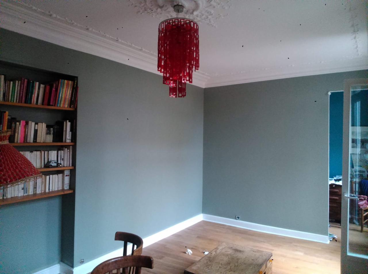 Pokój po odświeżeniu: ściany pomalowane na szaro, białe listwy przypodłogowe i sufitowe, drewniana podłoga, czerwony żyrandol, regał z książkami, drewniane krzesła. Widoczne niedoskonałości...