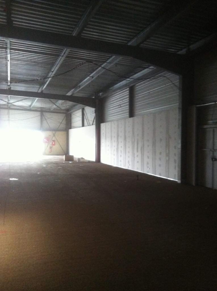 Wnętrze hali w trakcie adaptacji: widoczne płyty gipsowo-kartonowe na ścianach, stalowa konstrukcja dachu i podłoże w stanie surowym.