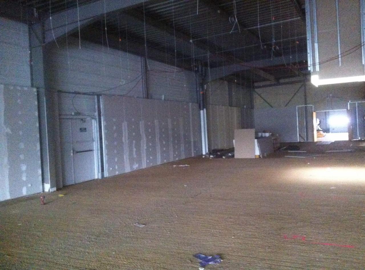 Wnętrze w trakcie wykańczania, ściany z płyt gipsowo-kartonowych z widocznymi łączeniami przed szpachlowaniem, surowy sufit z widoczną konstrukcją metalową, podłoga zabezpieczona folią.