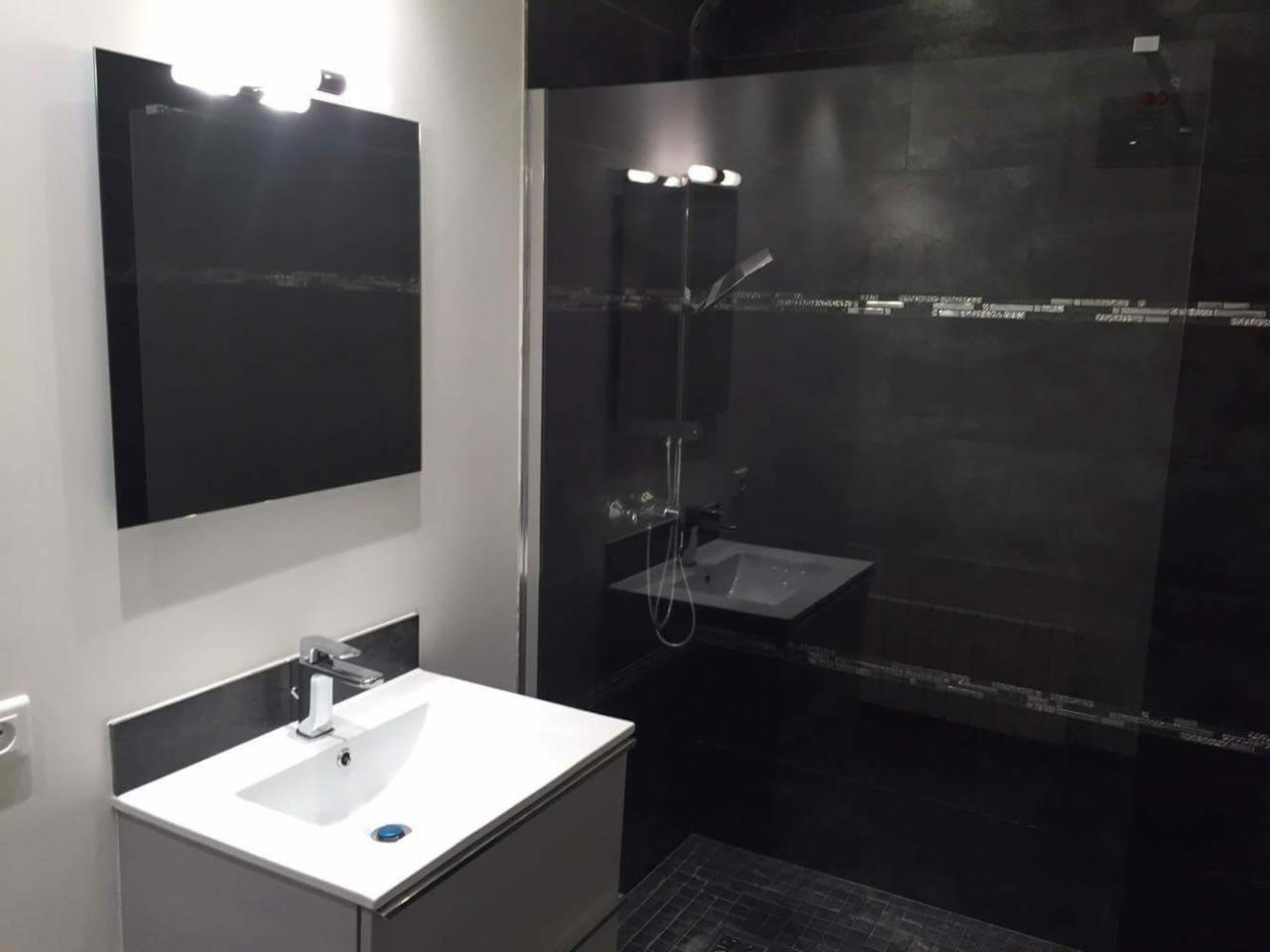 Nowoczesna łazienka w czarno-białej kolorystyce z umywalką, lustrem z oświetleniem i kabiną prysznicową z ciemnymi płytkami.