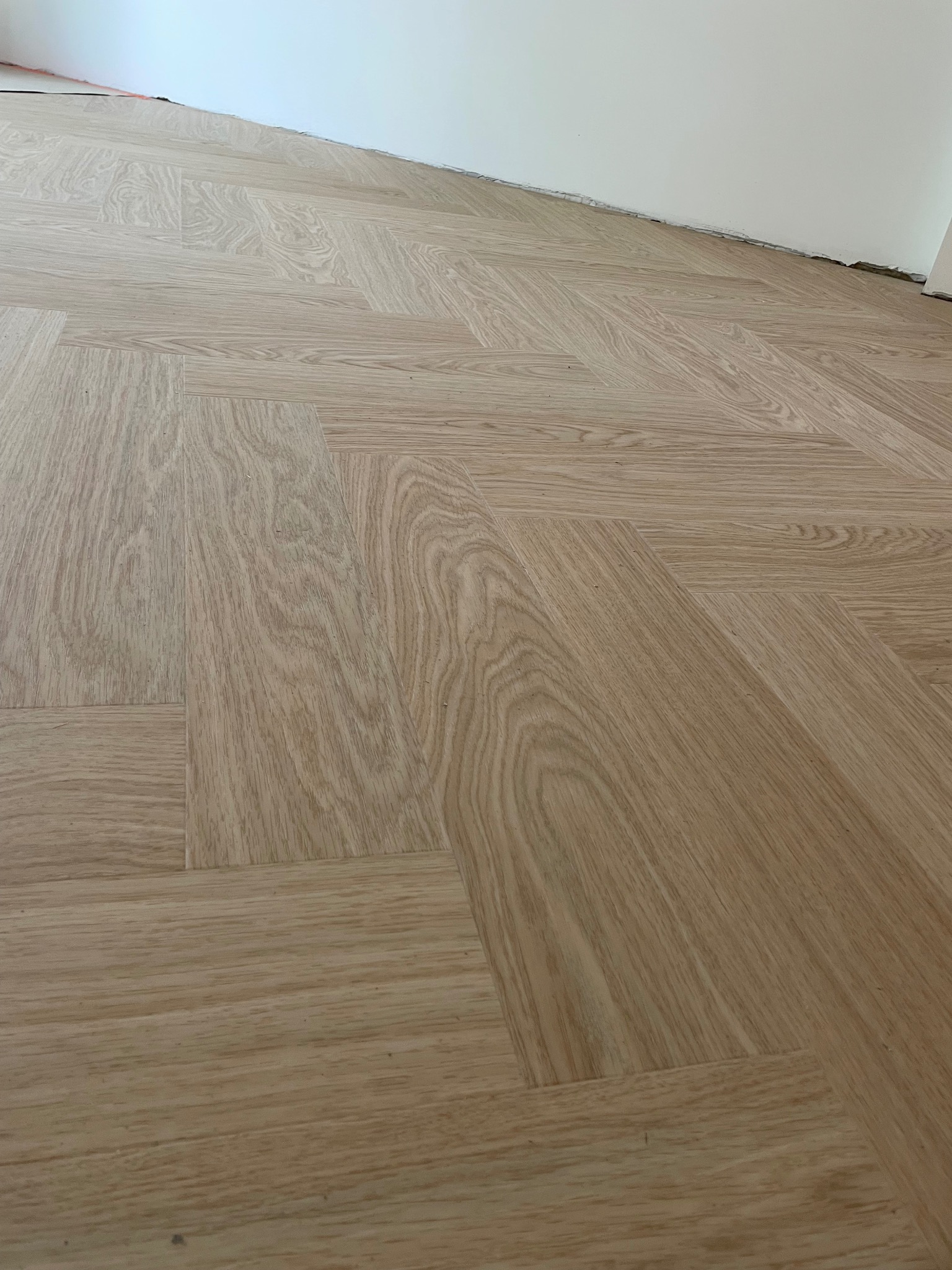 Ułożona podłoga winylowa Quick Step w jodełkę, model Dąb Rumiany Ciro, widoczne niedociągnięcia przy ścianie.