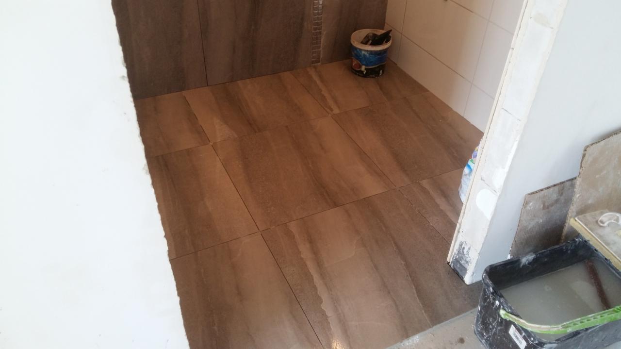 Układanie płytek podłogowych w łazience z widocznym wiaderkiem z zaprawą i narzędziami, etap prac wykończeniowych.