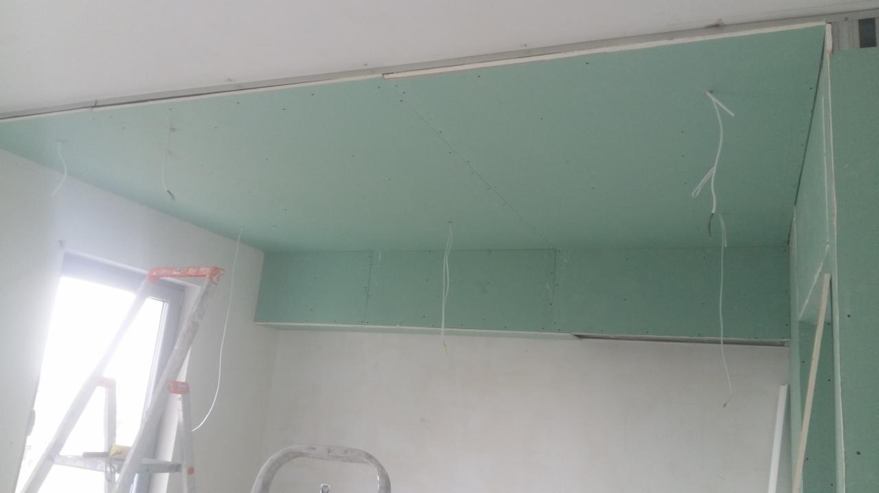Montaż sufitu podwieszanego z płyt gipsowo-kartonowych, widoczne kable elektryczne, drabina malarska przy oknie.