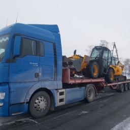 Usługi Transportowe - Niebieski ciągnik siodłowy MAN przewozi na niskopodwoziowej platformie żółto-czarną koparko-ładowarkę JCB na tle zimowego krajobrazu.