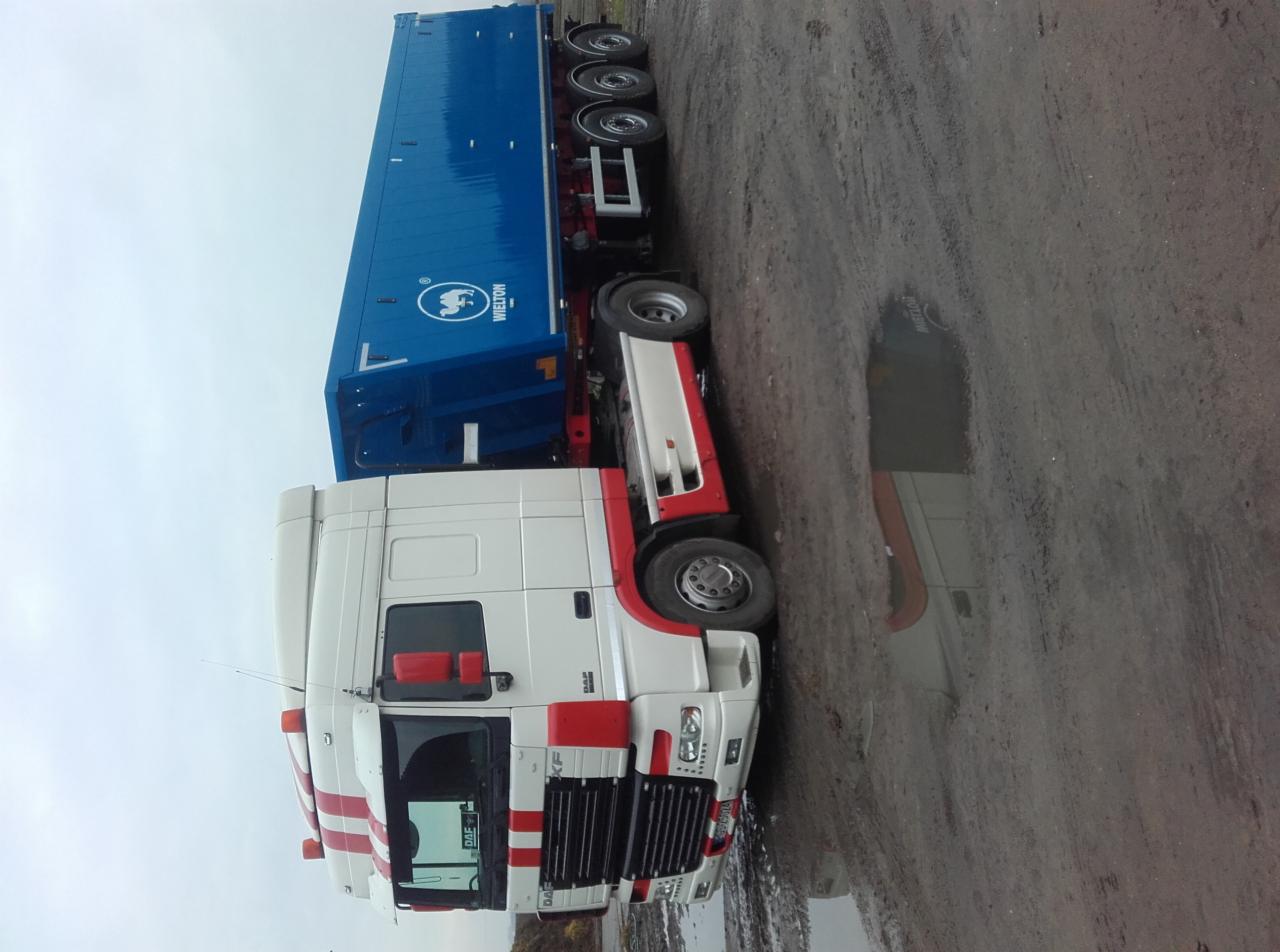 Ciężarówka DAF z naczepą Whelton na błotnistym placu, widoczne odbicie w kałuży.