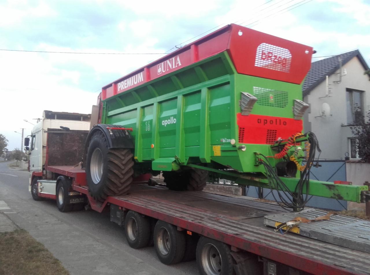 Ciężarówka DAF z naczepą przewożąca zielono-czerwony rozrzutnik obornika marki Unia Apollo.